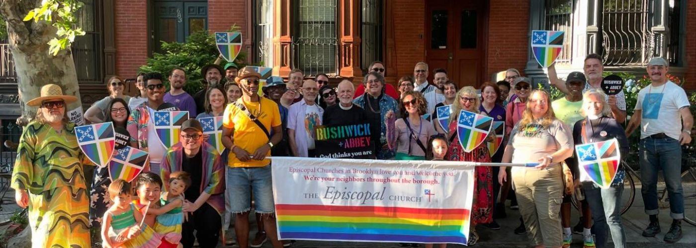 People marching at a Brooklyn Pride Parade holding an Episcopal Church Banner and Pride Episcopal Church Shields