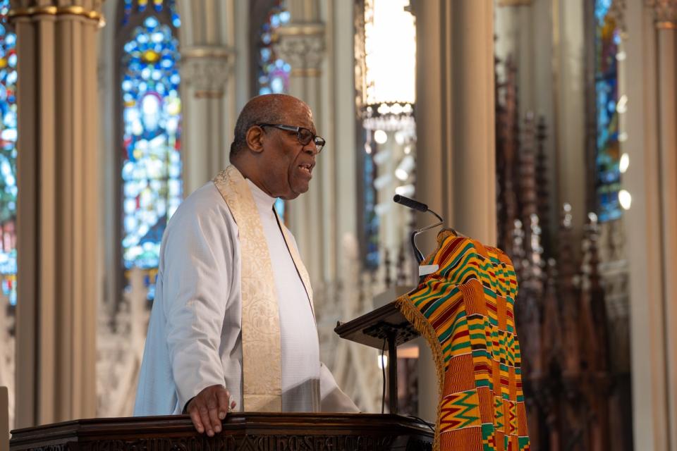 The Rev. Cn. Dr. Donald Kortright Davis delivers sermon in the pulpit of the Cathedral. Stained glass windows behind him. 