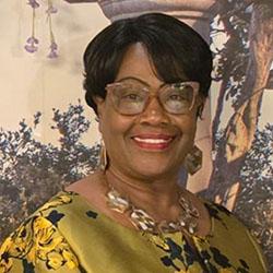 Headshot of Ancilla Friday, wearing glasses and large earrings