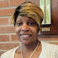 Headshot of Denise Grey-Stewart, wearing a white necklace and a white sweater