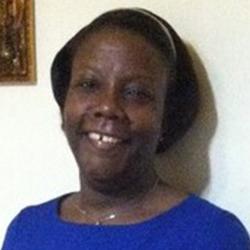 Headshot of Sheryl Edwards, standing near a wall, smiling, wearing a blue shirt.