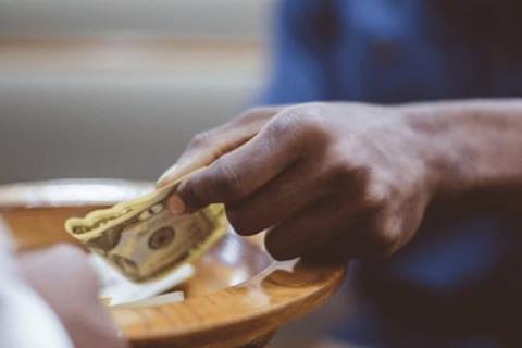 Person placing a $20 bill into a receiving plate