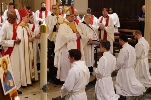 Four ordinands kneel facing the Bishop and other members of the clergy